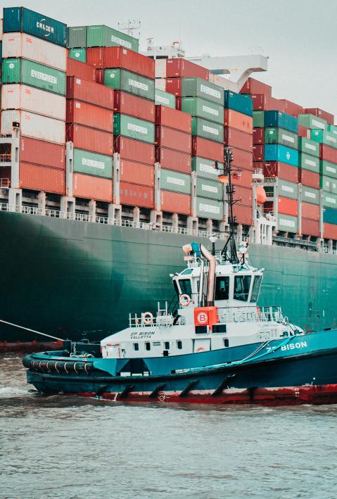 a tugboat crosses a large container ship