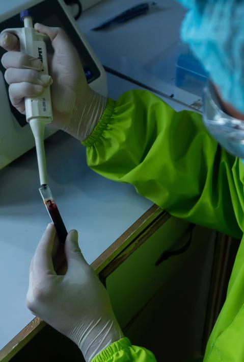 Researcher in protective suit takes sample with pipette. 
