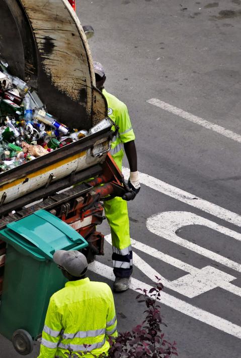 Cleaning staff in high-visibility vests emptying garbage cans with transporter. 