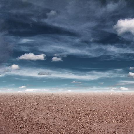 Graue Wolken hängen über karger Wüste. 