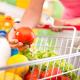 Full shopping cart at store with fresh vegetables and hands close-up